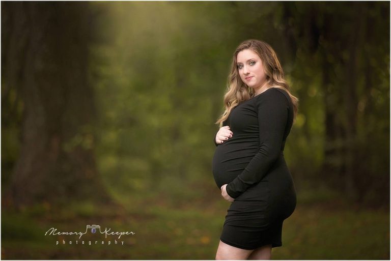 Pregnant mother to be in black dress embracing her belly